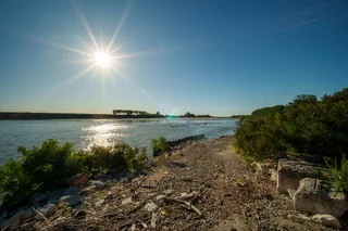 Sun over a wide river seen from a stony bank, Italy