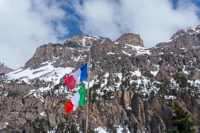 French and Italian flags below a snowy mountain face, France