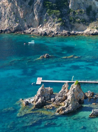 A swimmer diving off a jetty into a turquoise cove, Greece